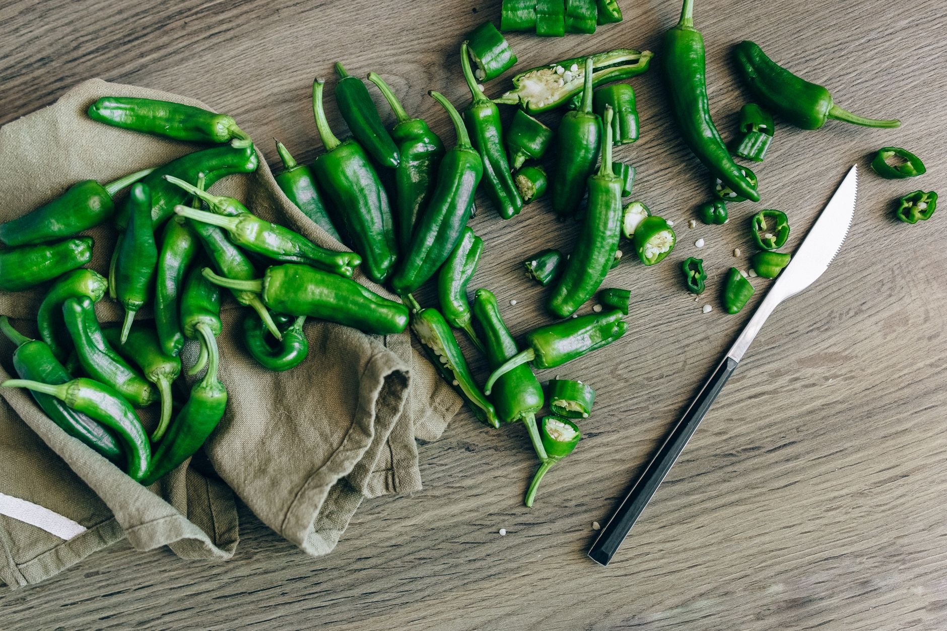 Green chili peppers scattered with knife on wooden surface, offering a rustic kitchen vibe.